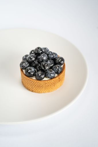 A vertical closeup of delicious tart with blueberries on top on white plate on light background