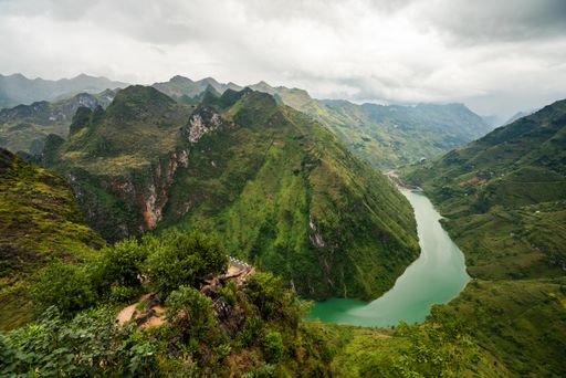 An aerial shot of a narrow river in the mountains under the cloudy sky in Vietnam
