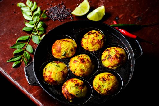 A pan with fried dish in designated small areas on a red marble table with spices and lime slices