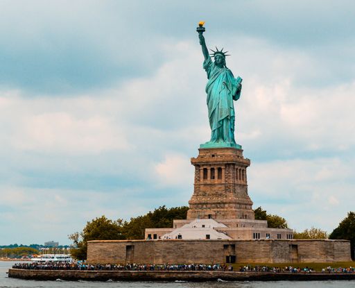 A scenic shot of the iconic Statue of Liberty in New York City, with crowds of people gathered around the base admiring the structure