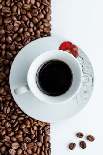 A vertical top view of a cup of coffee on a white table with coffee beans on it