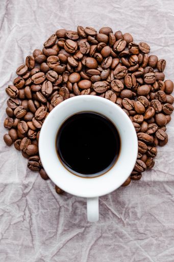 A vertical top view of a cup of coffee on a white table with coffee beans on it