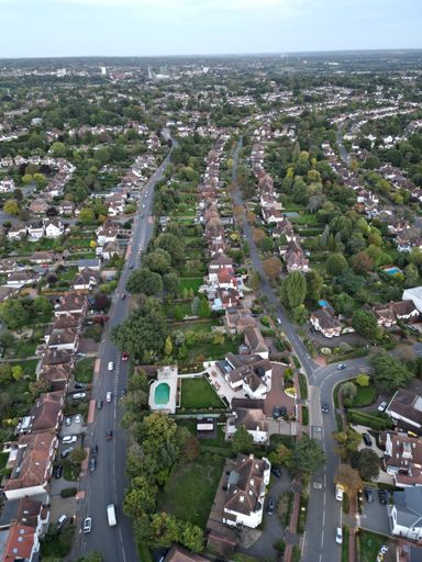 A high-angle shot of a city full of buildings, green trees, fields and roads at Bromley borough.
