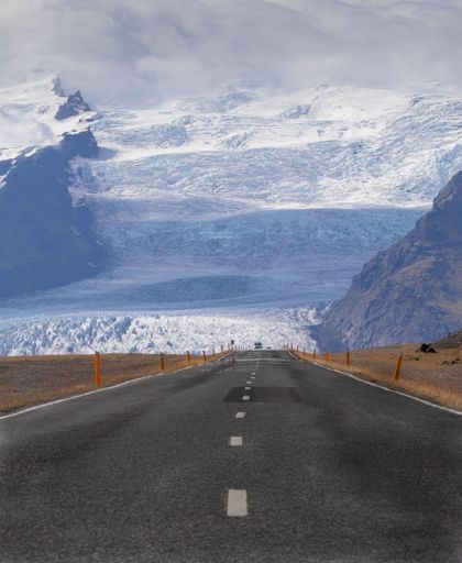 A vertical shot of the empty country road with snowy mountains in the background. Iceland.