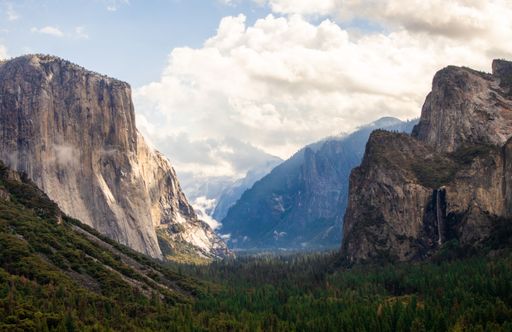 A scenic view of a valley surrounded by majestic mountain peaks in the distance in Yosemite National Park