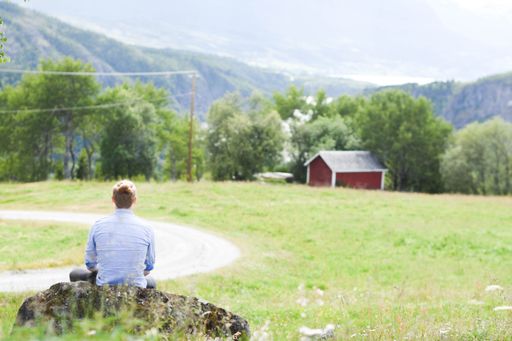 The young man enjoying the mountain landscape while sitting on the rocky stone, Valdres, Norway