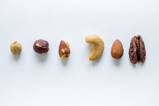 An overhead shot of different nuts in a line on a white surface