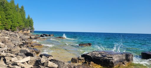 A panoramic shot of a beautiful sea with foamy waves crashing on a rocky beach