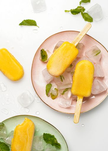 A vertical top view shot of mango ice cream popsicles on pastel-colored plates with ice.