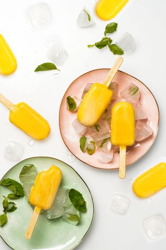 A vertical top view shot of mango ice cream popsicles on pastel-colored plates with ice.
