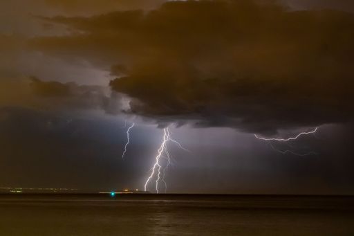 The lightning in a stormy night sky over a seascape hiding behind the clouds
