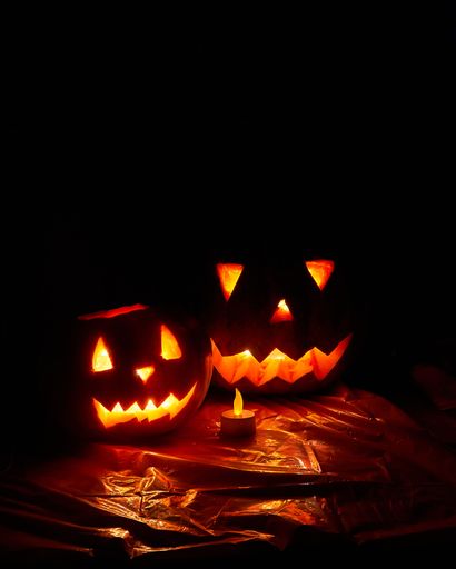 The spooky carved Halloween pumpkins and a candle burning on black background