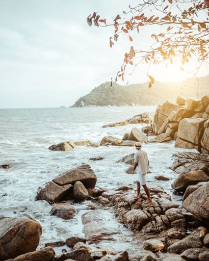 A back view of black man standing on rock formations by the beach in Thailand during sunset