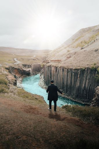 A back view of black man standing on the cliff overlooking the river in Iceland during sunset