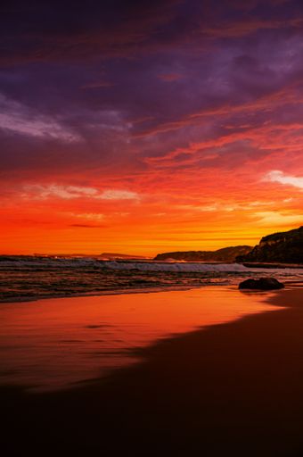 A vertical shot of calm sea waves moving towards the shore during a breathtaking sunset