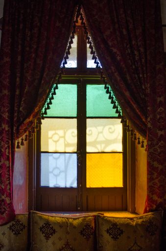 A vertical shot of a window sill with beautiful red and gold curtains and colorful glass