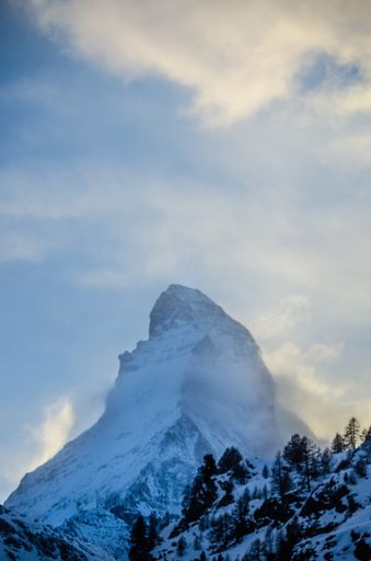 A vertical shot of a mountain covered in snow under the frozen winter sky