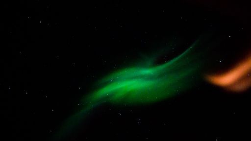 A scenic shot of green and orange colors of the Northern lights in the dark night sky