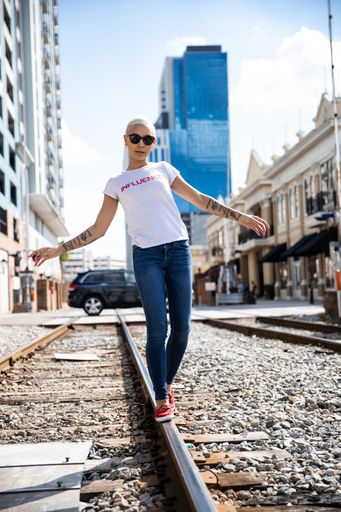 A vertical shot of a woman walking on a railroad track with city in the background