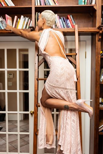 A woman wearing a long dress and reaching across the library to retrieve a book