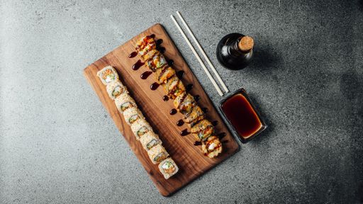 A top view of a set of delicious fresh sushi rolls, chopsticks, and soy sauce on a  wooden board
