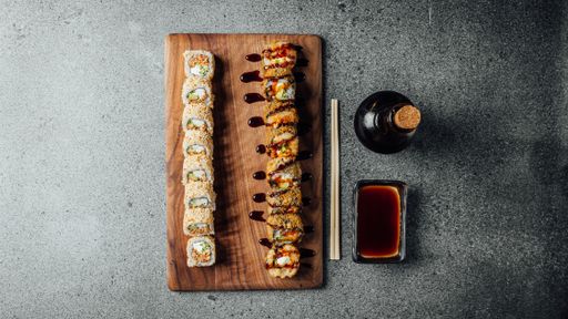 A top view of a set of delicious fresh sushi rolls, chopsticks, and soy sauce on a  wooden board