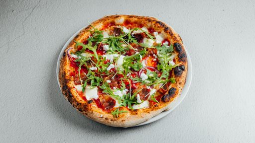 A top view of a pizza with tomato, mozzarella cheese and greens on a table