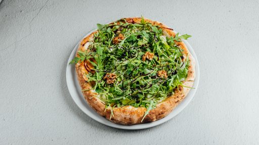 A delicious freshly baked homemade pizza with cheese, walnuts, and rucola on a white plate