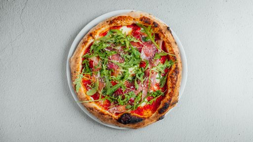 A top view of a pizza with arugula and prosciutto on a table