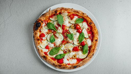 A top view of a pizza with greens, tomato and olives on a table