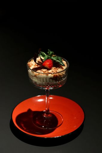 A vertical shot of a glass cup of ice cream with fruits on small plate  isolated on black background