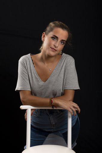 A vertical shot of a young beautiful blonde female posing on a chair with a black background