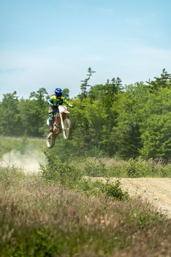 A vertical shot of a motocross racer taking a jump with trees in the background