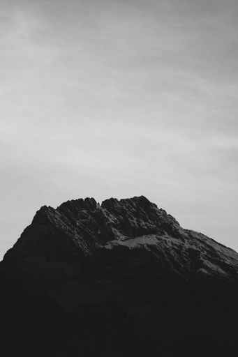 A vertical greyscale shot of peak of a rocky mountain covered with snow