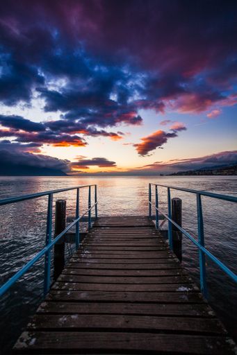 A beautiful shot of a wooden dock near the sea with the reflection of the sunset under the cloudy sky