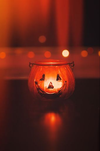 A vertical shot of a halloween candle  shaped like a Jack-o-Lantern on a blurred background