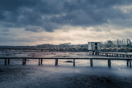 A dramatic shot of a boardwalk leading to a wooden cabin surrounded by trees under the storm clouds