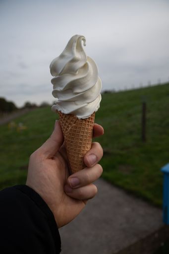 A vertical shot of a person holding an ice cream cone outdoors