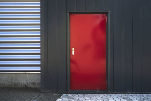 A building with black and silver walls and a red door on the pavement