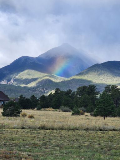 A vertical shot of a rainbow over the mountains in Colorado in the morning