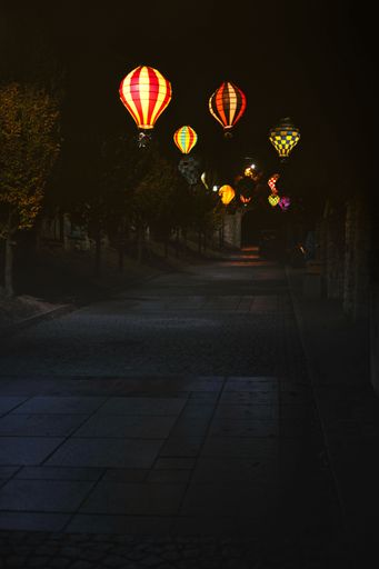 A vertical shot of an alley decorated with lit paper Chinese lanterns at night