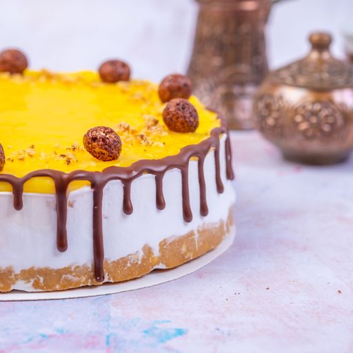 A closeup of the cheesecake with a yellow surface decorated with chocolate cream and chocolate balls on a blurry background