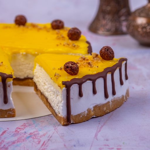 A closeup of the piece of a cheesecake with a yellow surface decorated with chocolate cream and chocolate balls on a blurry background