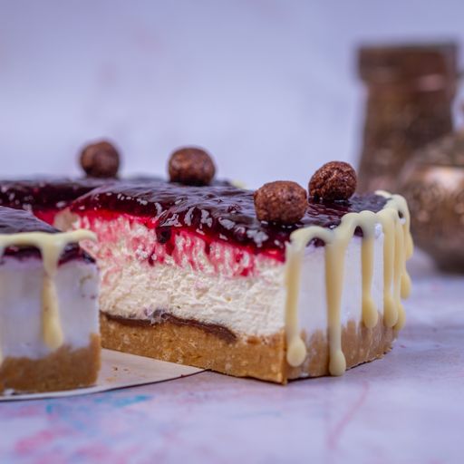 A closeup of the piece of the cheesecake with a jam surface decorated with vanilla cream and chocolate balls on a blurry background