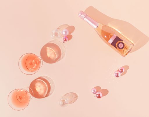 A top view of a pink champagne bottle and Christmas decoration against apricot color background-New Year party concept