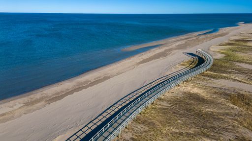 An aerial shot of a walkway on a beach against the blue sea on a sunny day