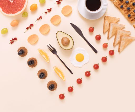 A flat lay of eggs, avocado, grapefruit, toast, cherry tomatoes, and waffles with black coffee, a breakfast concept