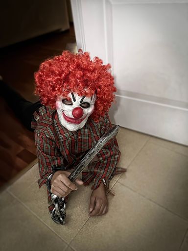 terrifying crazy clown lying on the floor with a smiling mask and a wig of curly red hair, hallowing costume, vertical