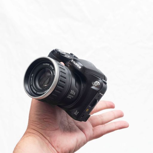 A person holding a Fujifilm Finepix s5200 compact camera on a white background