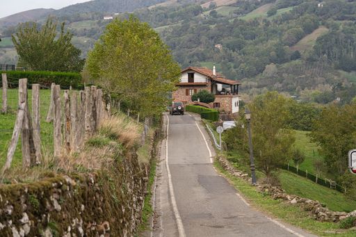 A hilly country road going up and down towards a house with green hills and trees behind the house in Erratzu, Spain